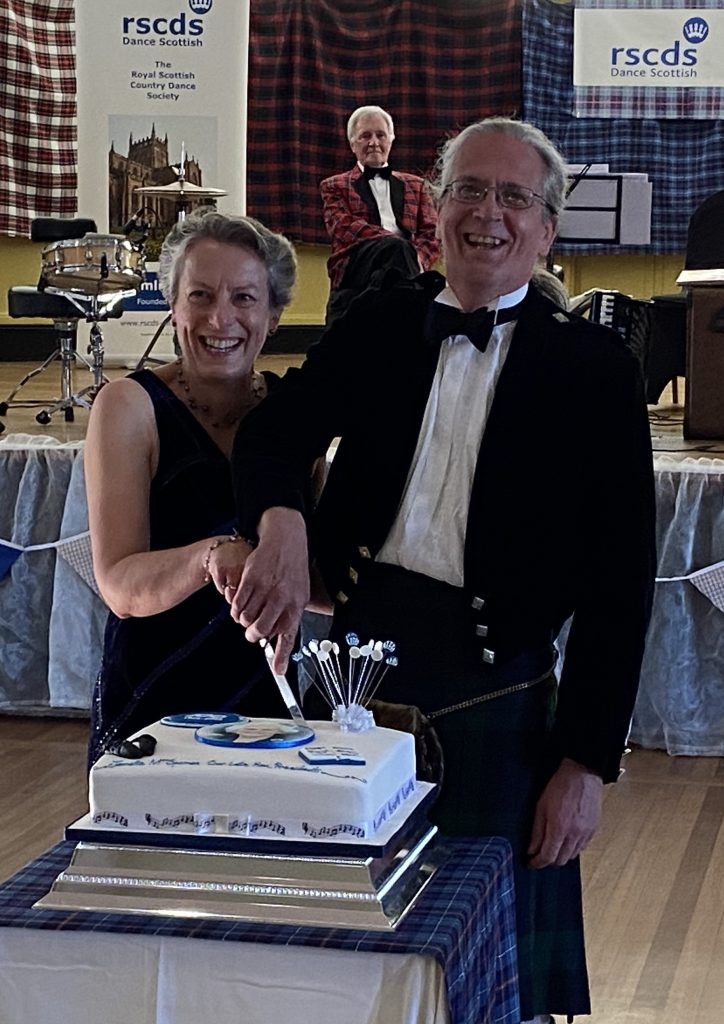 Nan and John cut the cake while musician Frank Thomson looks on.